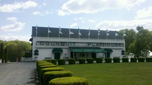 Ein weißes Gebäude mit der Aufschrift "OGUNQUIT PLAYHOUSE" und einem grünen Vordach. Vor der Fassade befinden sich ordentlich geschnittene Hecken.