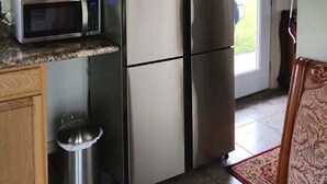 A compact kitchen with a stainless steel refrigerator, a microwave, and a trash bin.