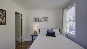 Ein Schlafzimmer mit einem Bett, einem Nachttisch, einer Lampe und einem Fenster mit Jalousien.