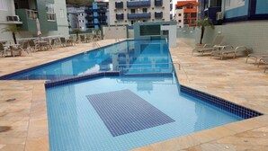 A swimming pool with tiled edges, surrounded by lounge chairs and a tiled deck. - Apt-207 in Comfortable Condominium 350m from the beach W/Air cond (Praia Grande)