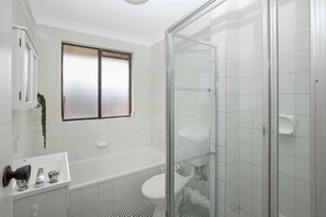 Et badeværelse med glasvæg omkring brusebad, badekar og toilet.