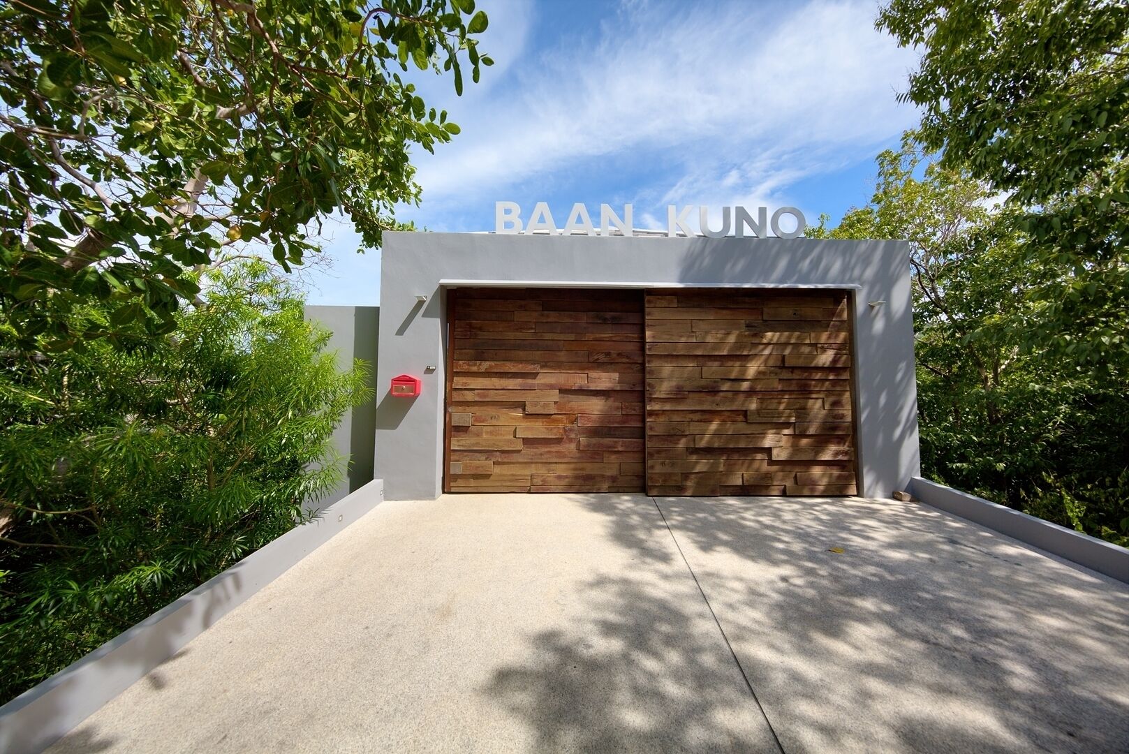 A modern building with a large wooden door and the name 'BAAN KUNO' above it.