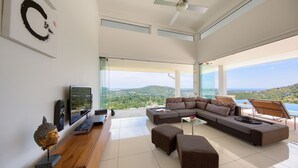 Un soggiorno moderno con un ampio divano componibile, una televisione a schermo piatto e un tavolino in legno. La stanza presenta ampie finestre con vista panoramica sulla campagna.
