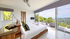 Una camera da letto moderna con un letto grande, un comodino con una lampada, una TV a parete e vista sul paesaggio attraverso ampie finestre.