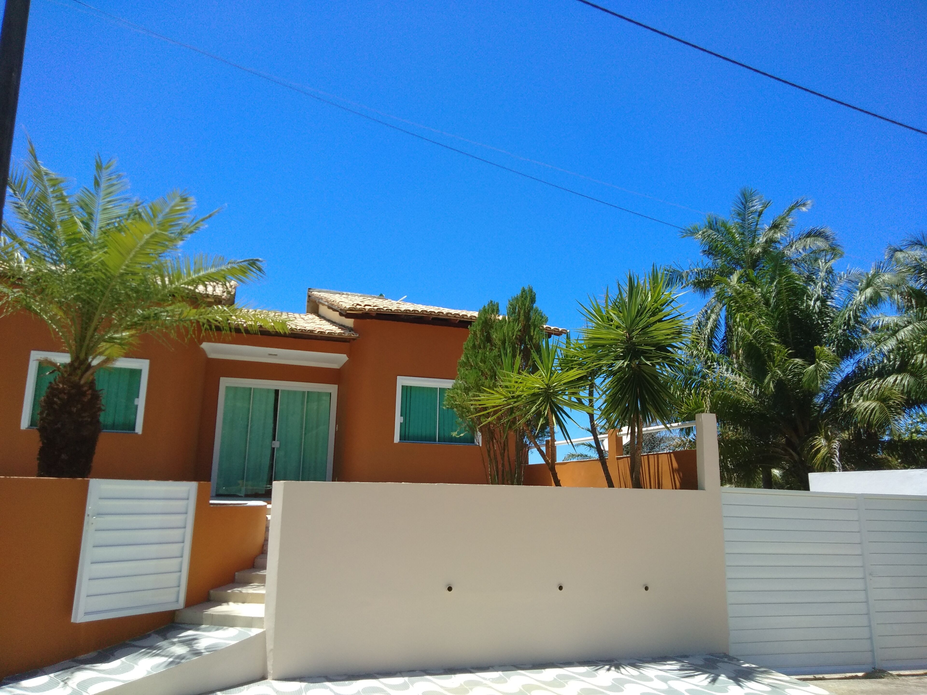 A residential building with a tiled roof, green shutters, and a white gate.