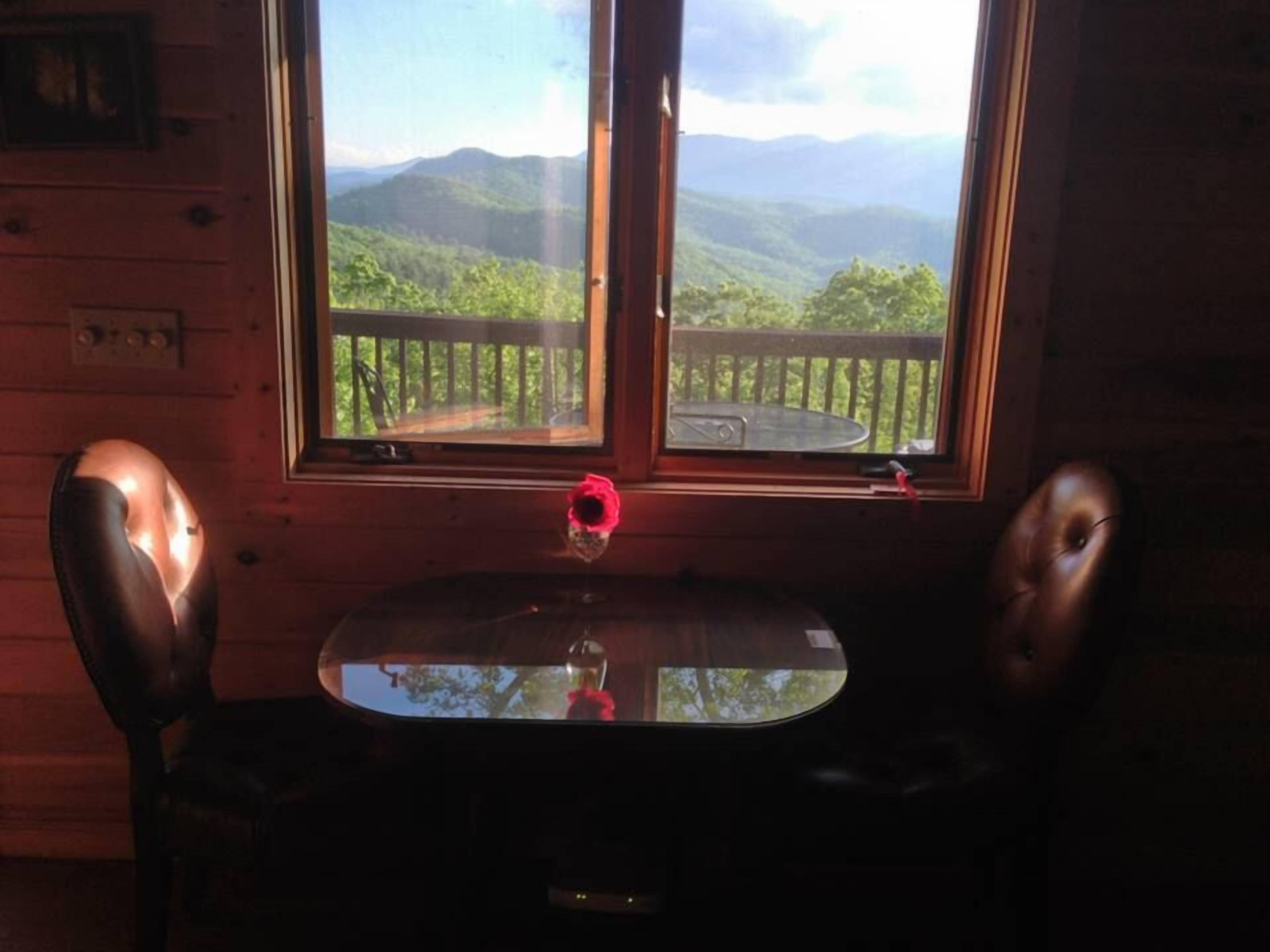 A room with a wooden interior, a table with chairs, a window with a view of mountains and a deck.