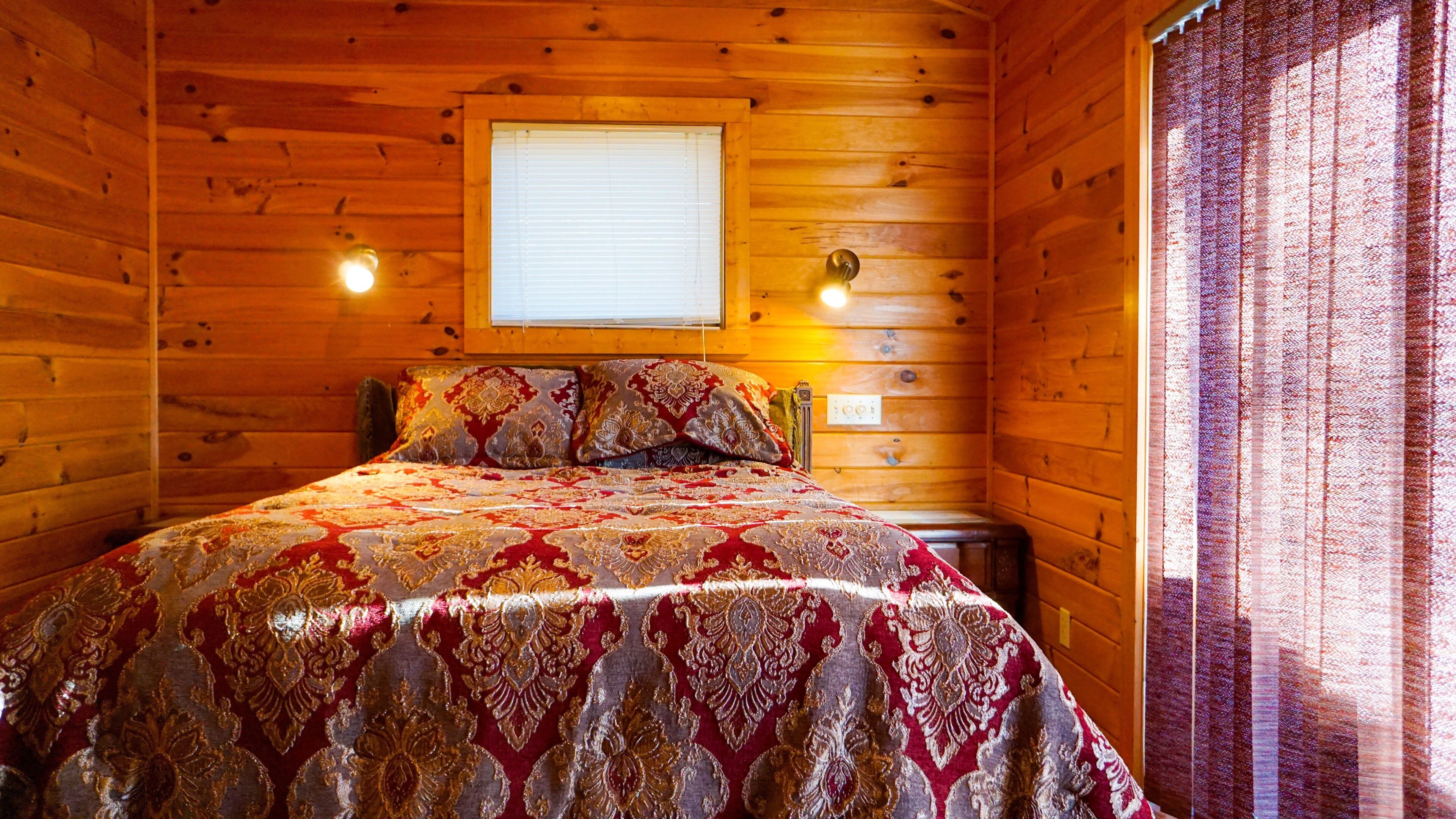 A wooden cabin room with a bed, a window, and two wall-mounted lights.