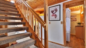 A wooden staircase with carpeted steps leading to a room with a white door, a framed picture, and a kitchen area visible through an open door. - Killington Cabin: Right Unit - Sleeps 10 in 4 BR, 2 BA Cozy Escape (Killington)