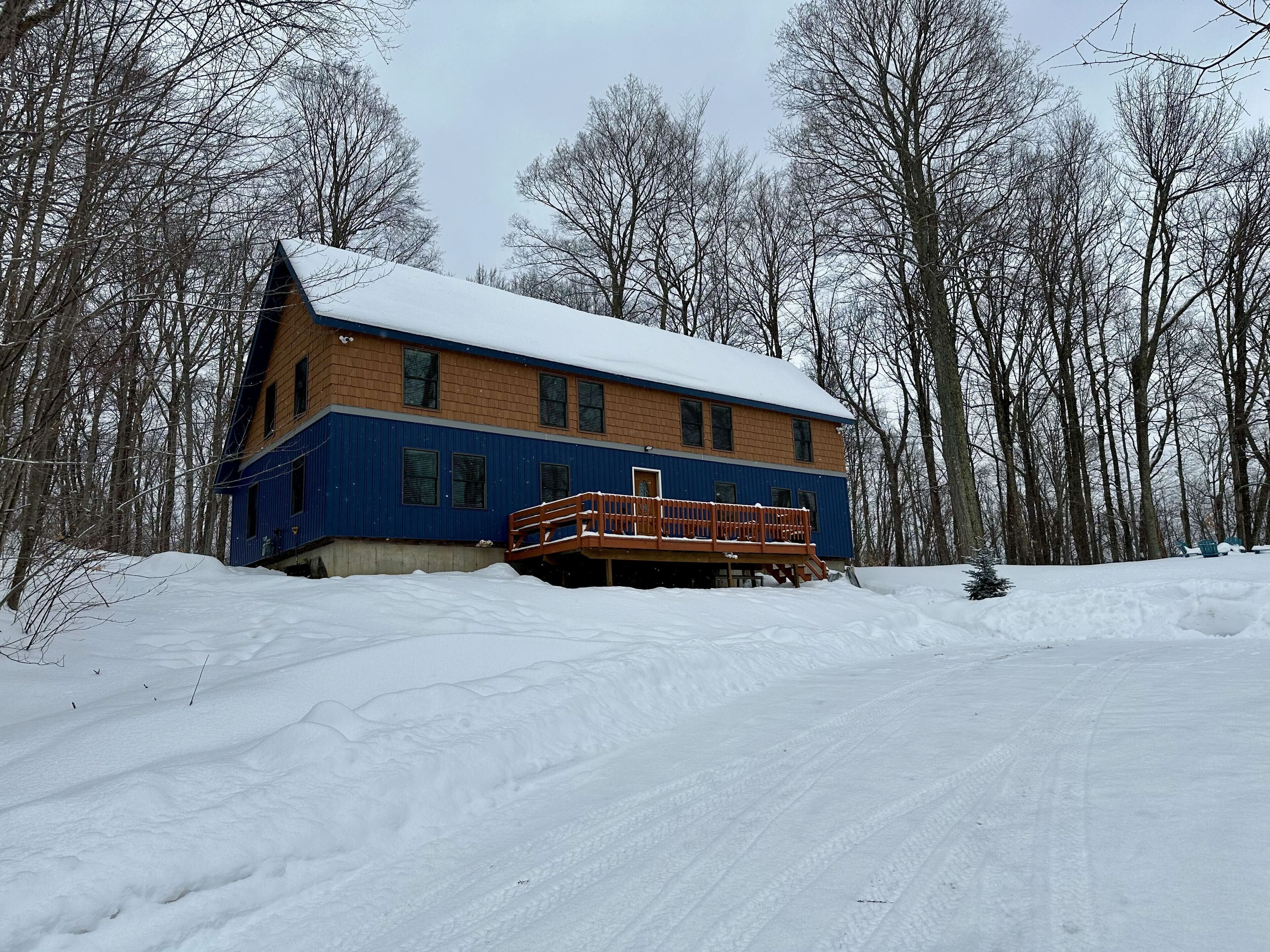 Una casa de dos pisos con techo nevado y un porche de madera.
