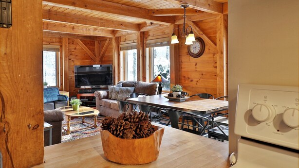 A cozy cabin interior with a wooden dining area, a sofa, a television, and a kitchen with a stove. - Killington Cabin: Right Unit - Sleeps 10 in 4 BR, 2 BA Cozy Escape (Killington)