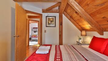 Un dormitorio con techo de madera, una cama litera, una mesita de noche con lámpara y un almohadón rojo.
