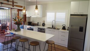 A modern kitchen with white cabinetry, a stainless steel refrigerator, and a bar area with stools.