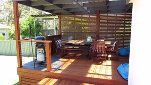 An outdoor patio with a wooden table and chairs, a grill, and a gas tank.