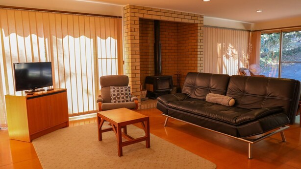A living room with a TV, leather sofa, wooden coffee table, and a brick fireplace. - Leafy Long Beach Hideaway (LONG BEACH)