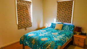 A bedroom with a bed, two bedside tables, a nightstand, and a window with patterned curtains. - Leafy Long Beach Hideaway (LONG BEACH)