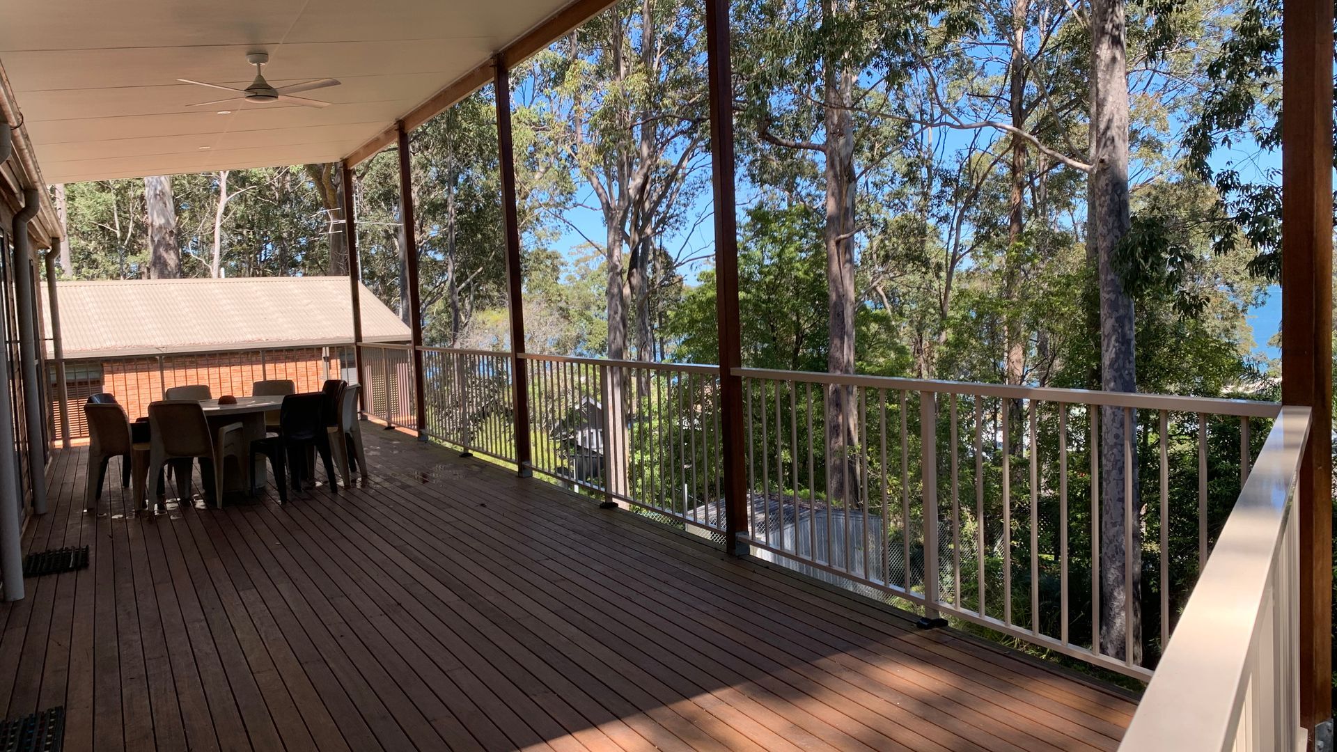 A covered outdoor deck with a table and chairs, surrounded by trees.