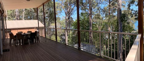 A covered outdoor deck with a table and chairs, surrounded by trees.