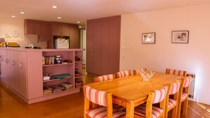 A dining area with a wooden table and striped chairs, a pink cabinet with books and kitchen items, and a large pink cupboard in the background. - Leafy Long Beach Hideaway (LONG BEACH)