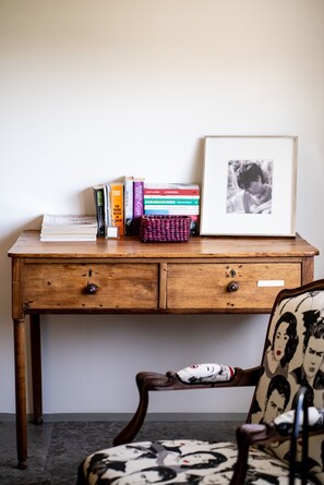 A wooden desk with books, a framed picture, and a chair with a patterned cushion.
