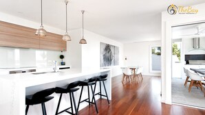 A modern kitchen with a white countertop, black bar stools, and pendant lighting. - Luxury in Corlette - 4 Drungall Ave - Beautiful Home with Air Con and WiFi (CORLETTE)