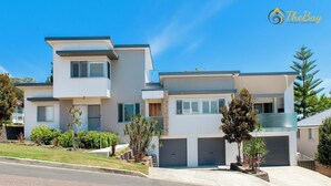 A modern two-story house with a garage, a balcony, and a well-maintained lawn. - Luxury in Corlette - 4 Drungall Ave - Beautiful Home with Air Con and WiFi (CORLETTE)