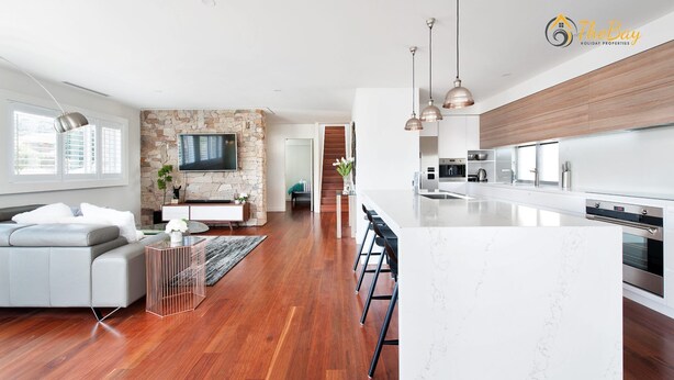 A modern kitchen with a large island, a dining area with bar stools, and a living room with a sofa and TV. - Luxury in Corlette - 4 Drungall Ave - Beautiful Home with Air Con and WiFi (CORLETTE)