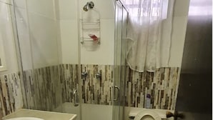 Un baño con ducha envuelta en vidrio, un lavabo y dos inodoros.