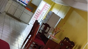 Un comedor con una mesa, sillas, un refrigerador y un ventanal con un calendario.