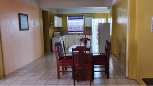 Una cocina compacta con comedor, con piso de baldosas, un refrigerador, un microondas y un ventanal con cortina colorida.