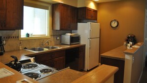 A compact kitchen with wooden cabinets, a microwave, a refrigerator, a sink, and a stove. - Mountain Harbor #205 3 Bedroom Condo (Whitefish)