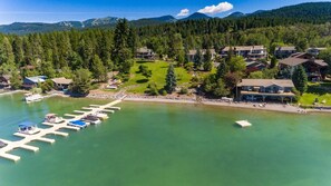 An aerial view of a lakeside resort with docked boats, a golf course, and residential buildings. - Mountain Harbor #205 3 Bedroom Condo (Whitefish)