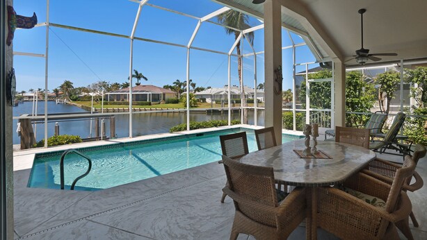 A covered outdoor area with a pool, wicker furniture, and a view of a marina. - Family Friendly perfect place to make memories! (Marco Island)