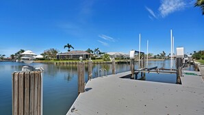 A waterfront dock with a wooden walkway, a small boat docked, and a clear blue sky. - Family Friendly perfect place to make memories! (Marco Island)