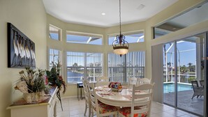 A dining area with a large table, chairs, and a view of a swimming pool. - Family Friendly perfect place to make memories! (Marco Island)