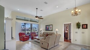 A spacious living room with a ceiling fan, a beige sofa, a red leather chair, and a coffee table. - Family Friendly perfect place to make memories! (Marco Island)