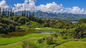 Ein Golfplatz mit Teich, umgeben von üppiger Vegetation und Bergen.