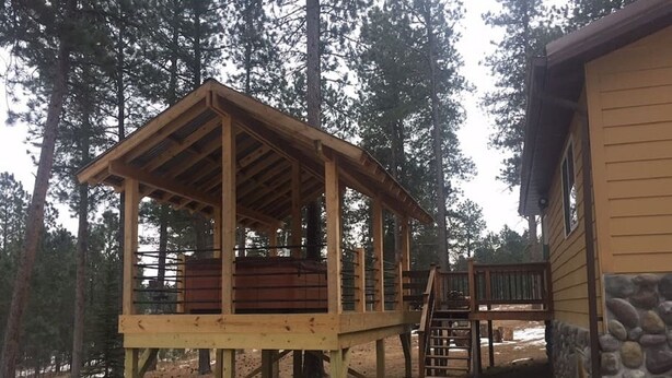 En träkonstruerad terrass med ett takbeklätt sittområde, en stenmur och en gångväg som leder till ett hus.