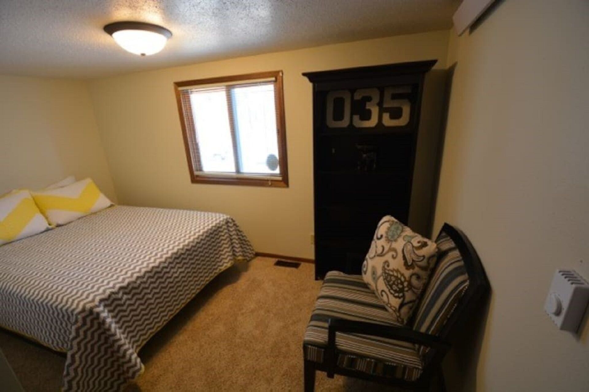 A bedroom with a bed, a chair, a window, and a door with the number 035.