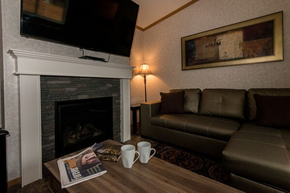 A living room with a fireplace, a sofa, a coffee table with a magazine and mugs, a TV, and a lamp. - C&C Home -Rural, Private, Fire Place, Quality (Nelson)