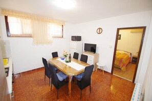 A compact room with a dining table, chairs, a microwave, a TV, and a bed with a colorful bedspread.
