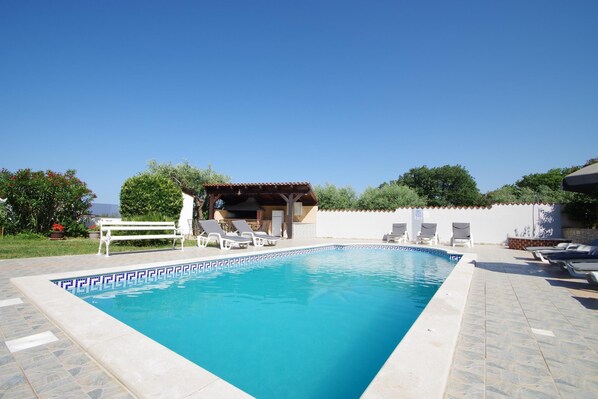Une piscine rectangulaire dont le bord est recouvert de carreaux, entourée de chaises longues et d’un espace de détente abrité.