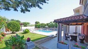 Un patio trasero con piscina, mobiliario exterior y plantas en macetas.