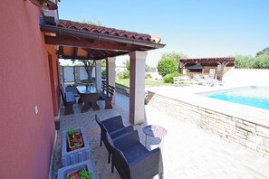 An outdoor patio with wicker furniture, a pool, and a covered area with a tiled roof.