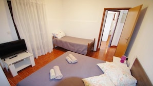 Una habitación de hotel con una cama, un televisor en un mueble bajo, una mesita y una puerta que da a otra habitación.