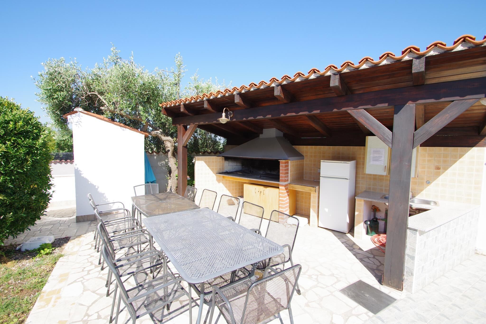 Un patio al aire libre con una mesa y sillas de metal, una parrilla y una pequeña área de cocina con refrigerador.
