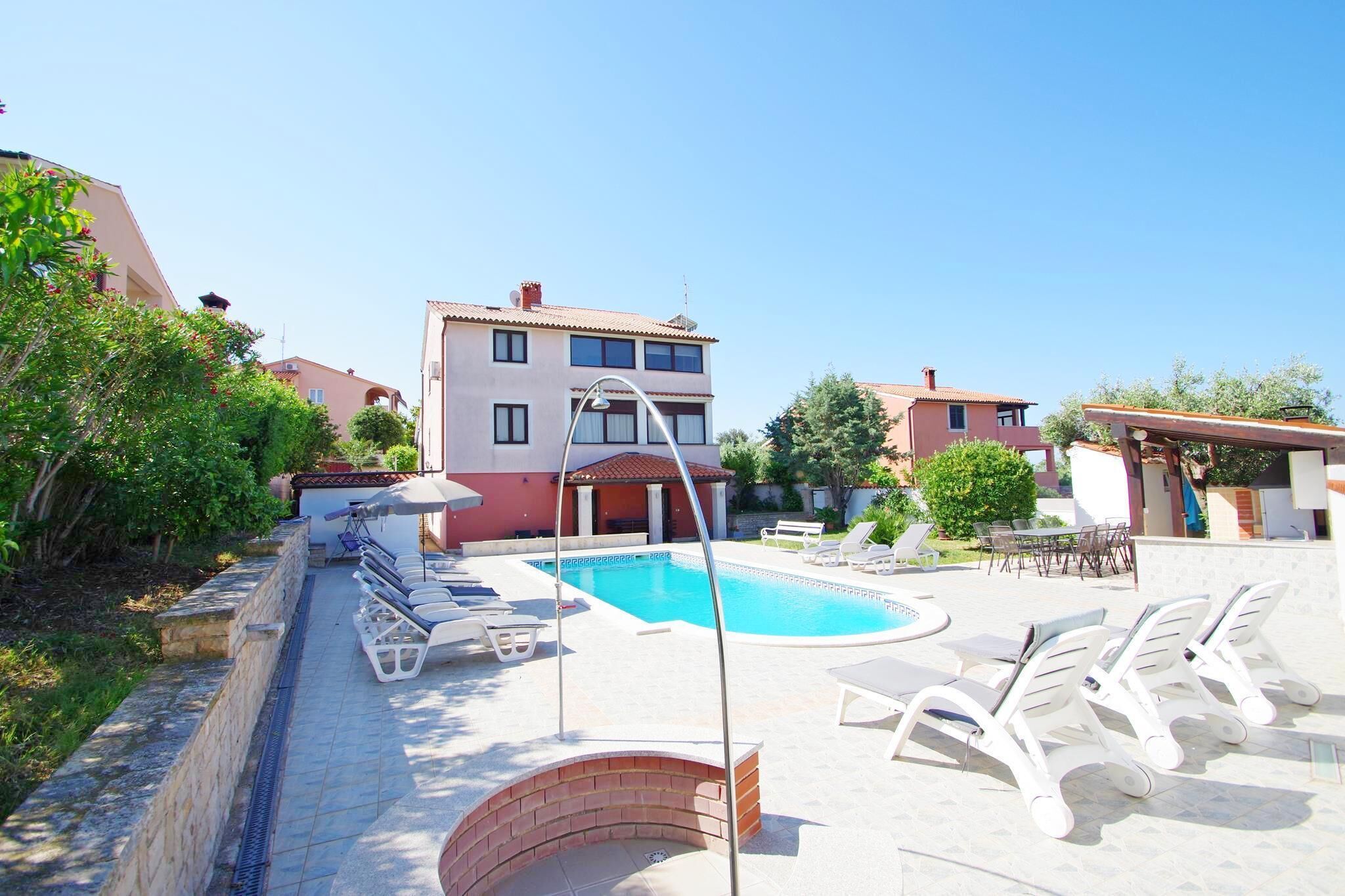 A swimming pool with lounge chairs, a brick wall, and a building with balconies in the background.