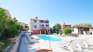 Una piscina con sillones de descanso, un muro de ladrillo y un edificio con balcones al fondo.