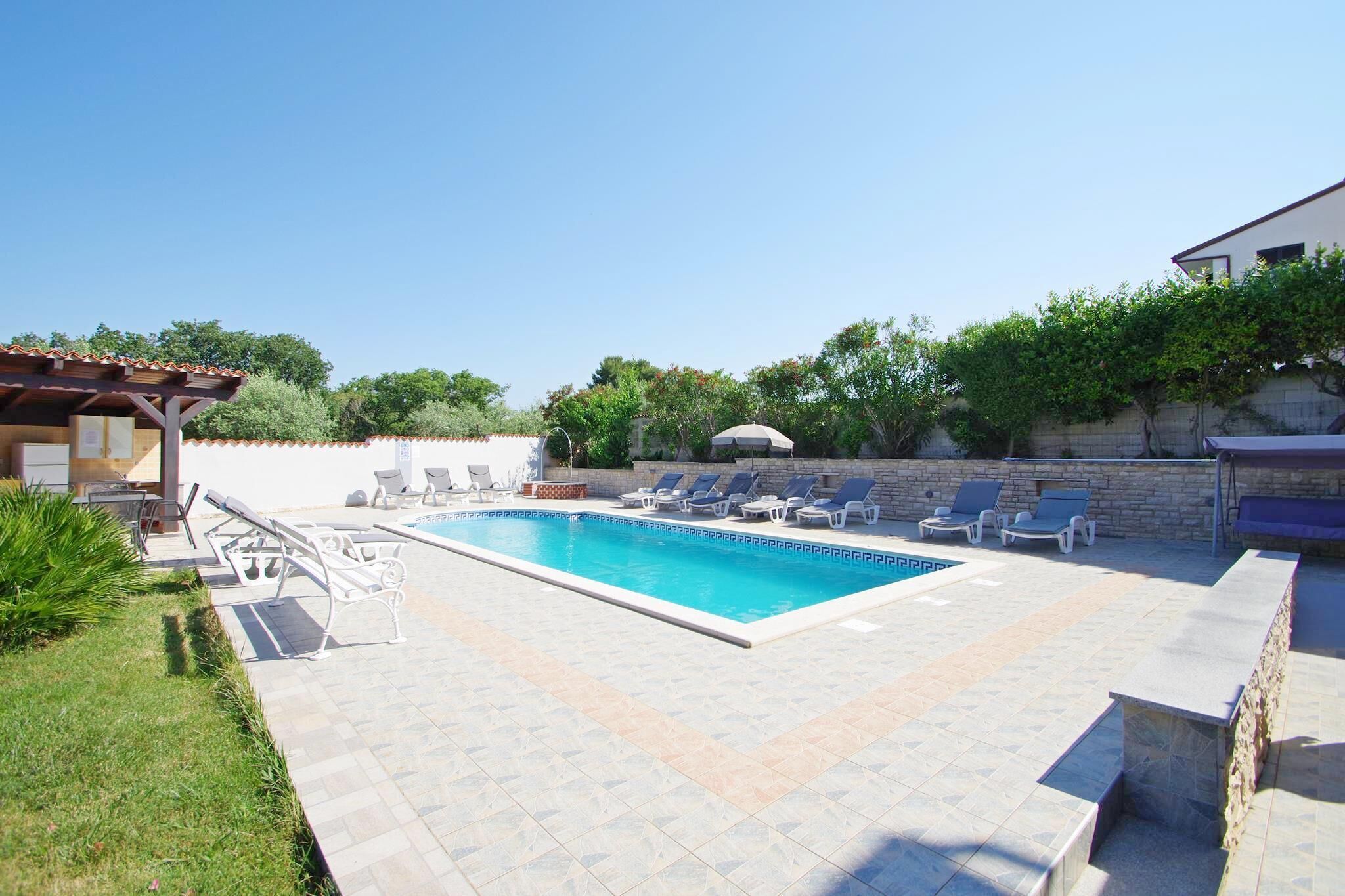 Ein rechteckiger Pool mit gefliestem Sonnendeck, umgeben von Liegestühlen und einer Pergola.