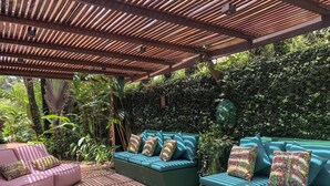 A covered outdoor seating area with two sofas and a bench, surrounded by lush greenery and a wooden pergola. - House 50m from the beach in a unique gated community, total privacy, Camburizinho.  (Sertão do Cambury)