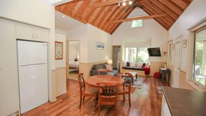 Eine geräumige Küche mit Holzboden, ein Essbereich mit Holztisch und Stühlen, ein Wohnzimmer mit Sofa und Fernseher sowie eine hohe Decke mit freiliegenden Balken.